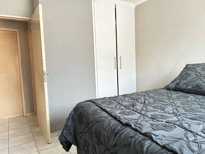 A bedroom featuring tiled flooring and a built-in wardrobe with white doors, providing functional storage space.