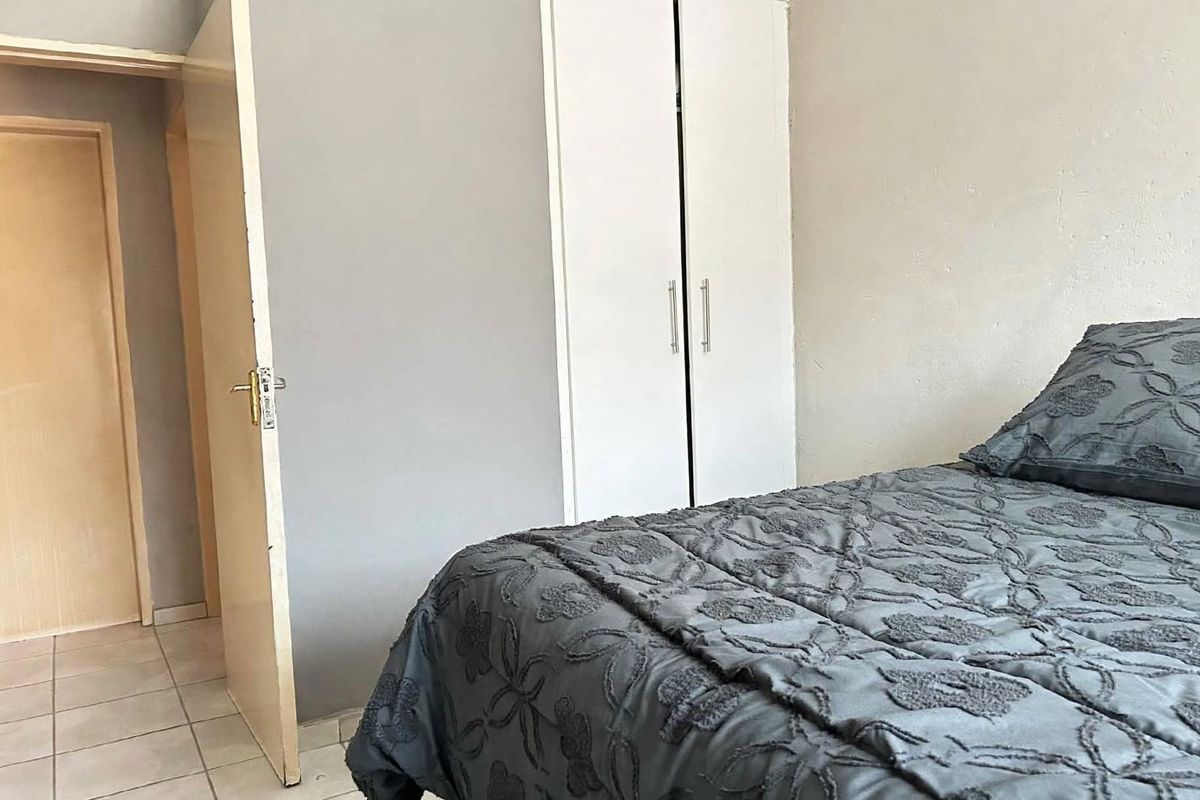 A bedroom featuring tiled flooring and a built-in wardrobe with white doors, providing functional storage space.
