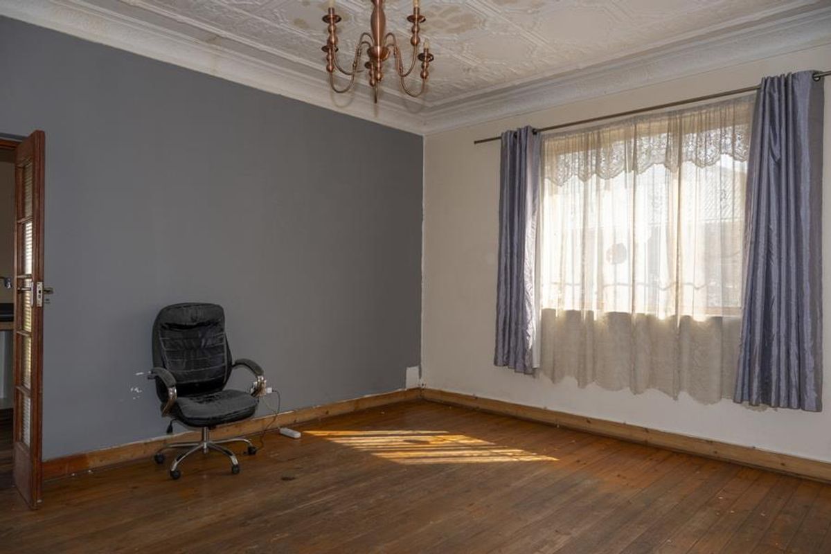 A sparsely furnished living room featuring original timber flooring, decorative ceiling molding, and a large window with natural light.