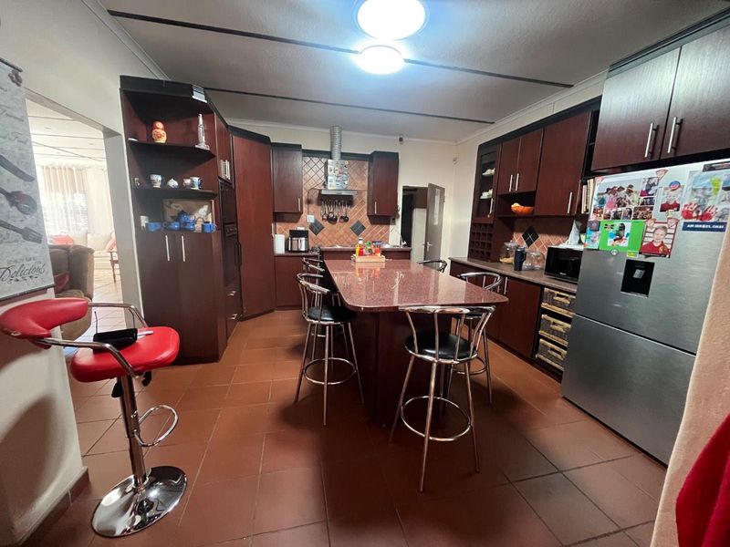 Spacious kitchen featuring dark wood cabinetry, a central granite island with breakfast bar seating, and tiled flooring throughout.