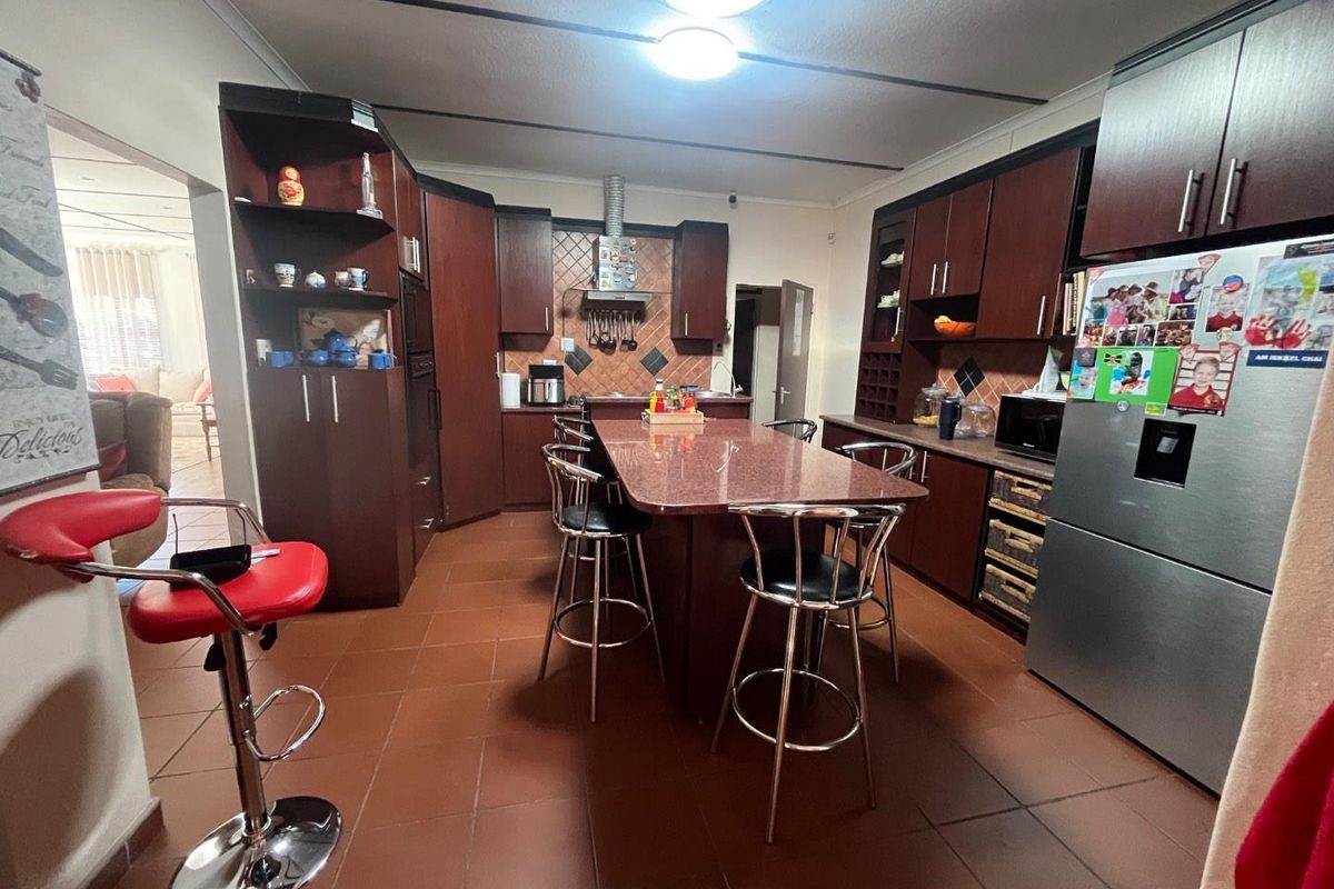 Spacious kitchen featuring dark wood cabinetry, a central granite island with breakfast bar seating, and tiled flooring throughout.