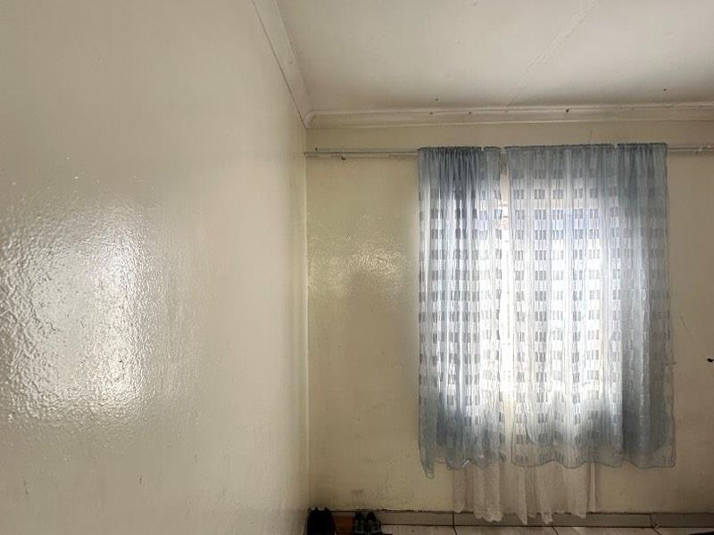 A simple bedroom featuring tiled flooring, white walls with cornice detailing, and a window fitted with a curtain rod.