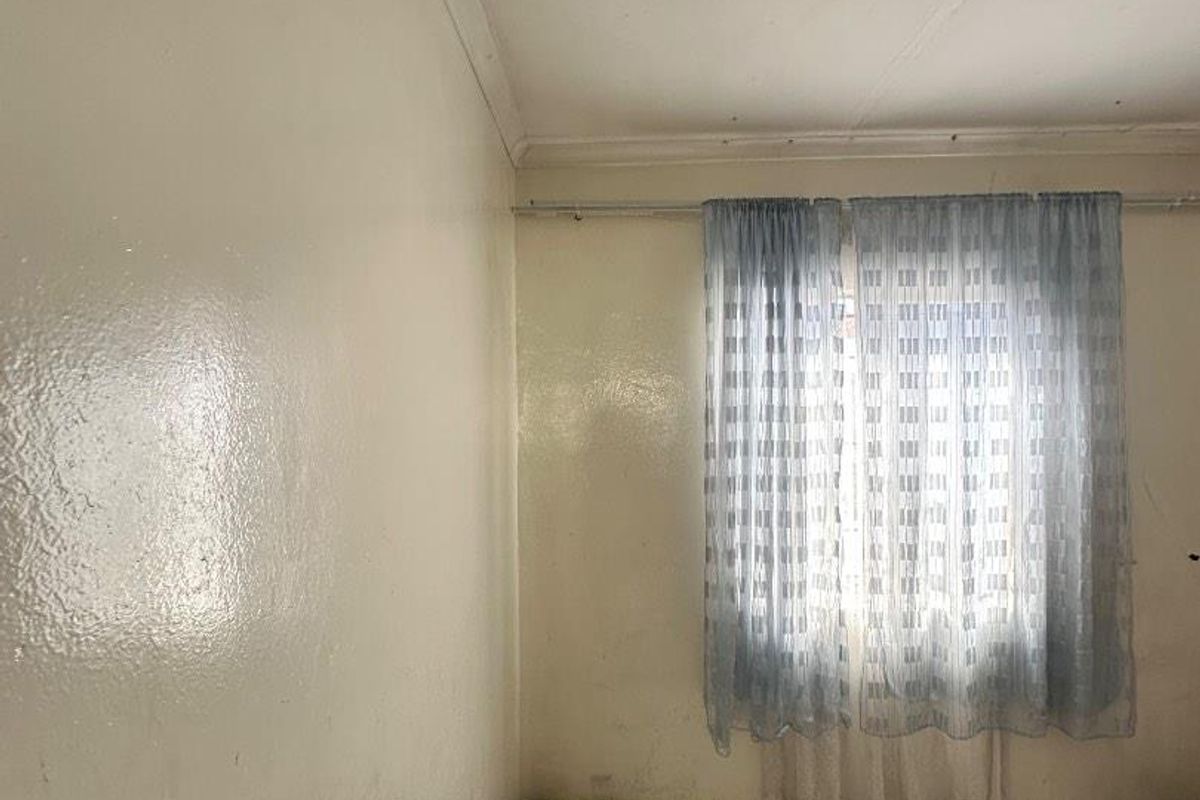 A simple bedroom featuring tiled flooring, white walls with cornice detailing, and a window fitted with a curtain rod.