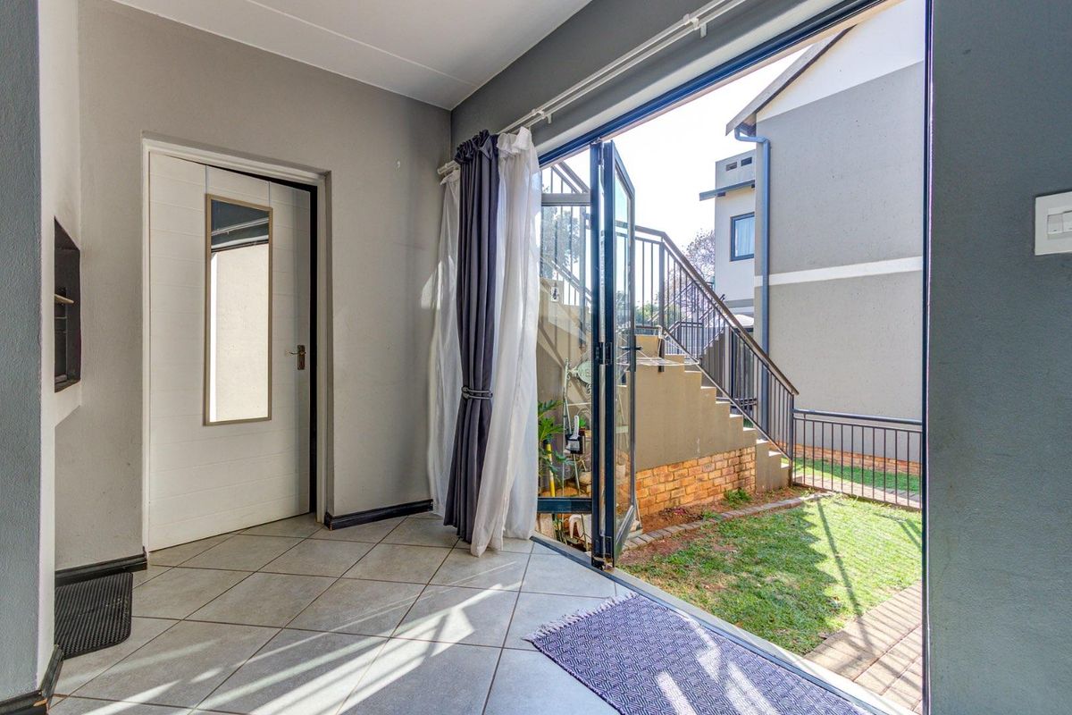 A bright interior space featuring tiled flooring and large glass doors opening onto a private garden area with external stairs.