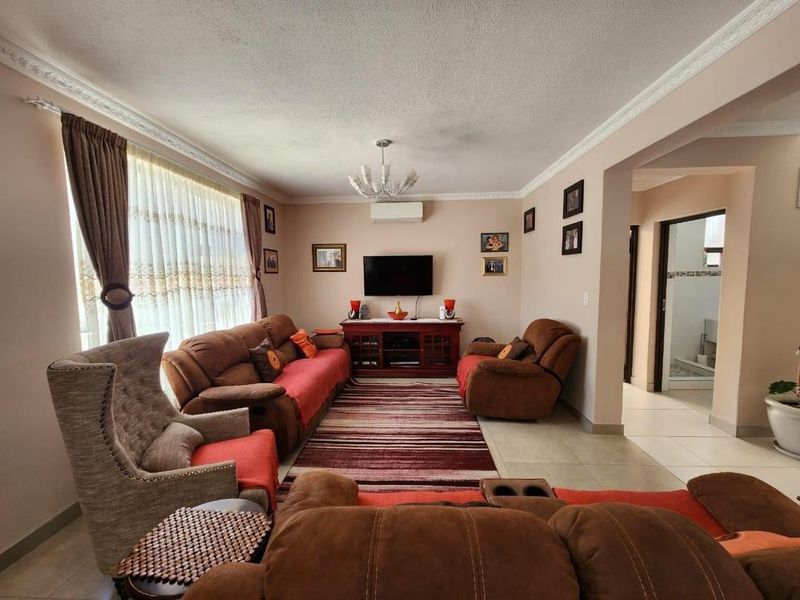 A spacious living room featuring tiled flooring, decorative ceiling cornices, and a wall-mounted air conditioning unit, providing a comfortable and functional living space.