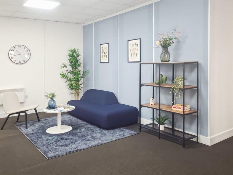 A modern office space featuring a clean, professional aesthetic with a blue accent wall, suspended ceiling, and integrated wall-mounted heating.