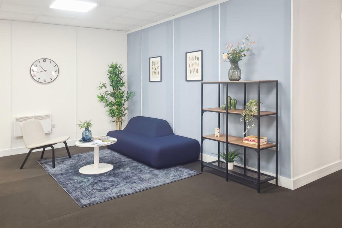 A modern office space featuring a clean, professional aesthetic with a blue accent wall, suspended ceiling, and integrated wall-mounted heating.