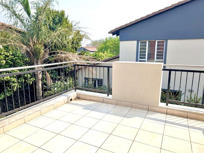 An open-air balcony featuring tiled flooring and a secure metal balustrade, offering a private outdoor space with views of the surrounding greenery.