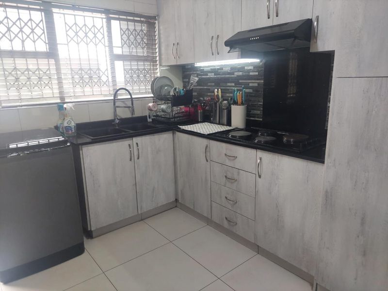 A functional kitchen featuring light wood-grain cabinetry, black granite countertops, a built-in electric hob with extractor fan, and tiled flooring.