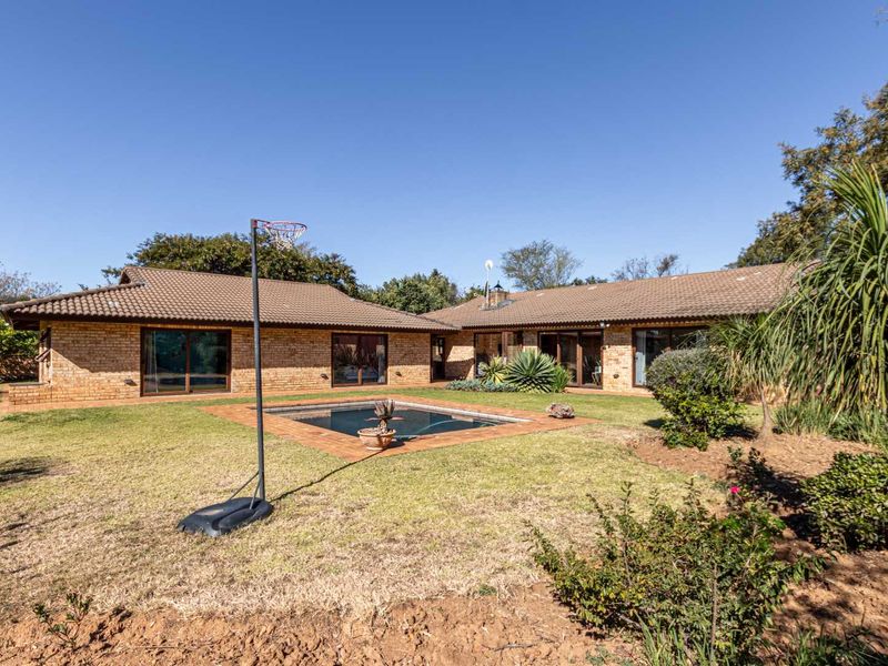 Rear view of a single-story brick house featuring a swimming pool, paved surround, and sliding glass doors opening onto the garden.