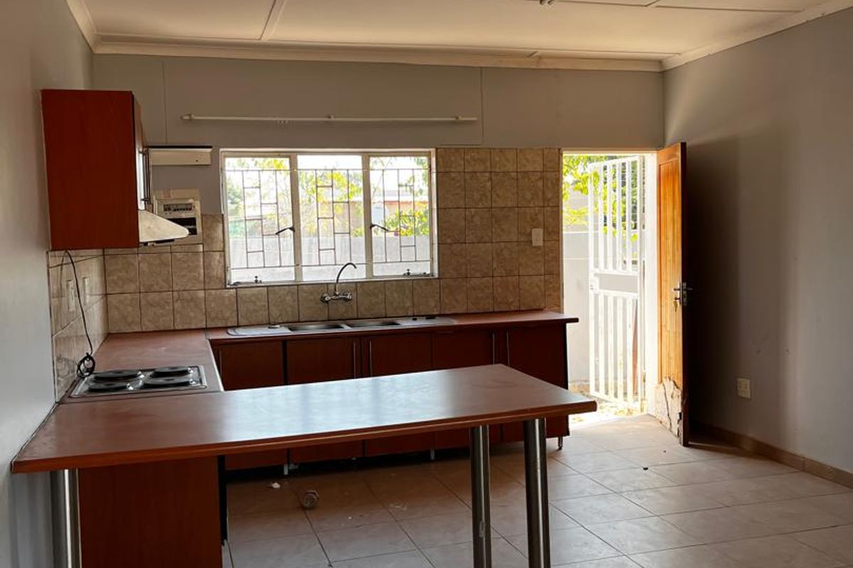 A functional kitchen featuring built-in cabinetry, a breakfast bar, tiled splashbacks, and direct access to the exterior.