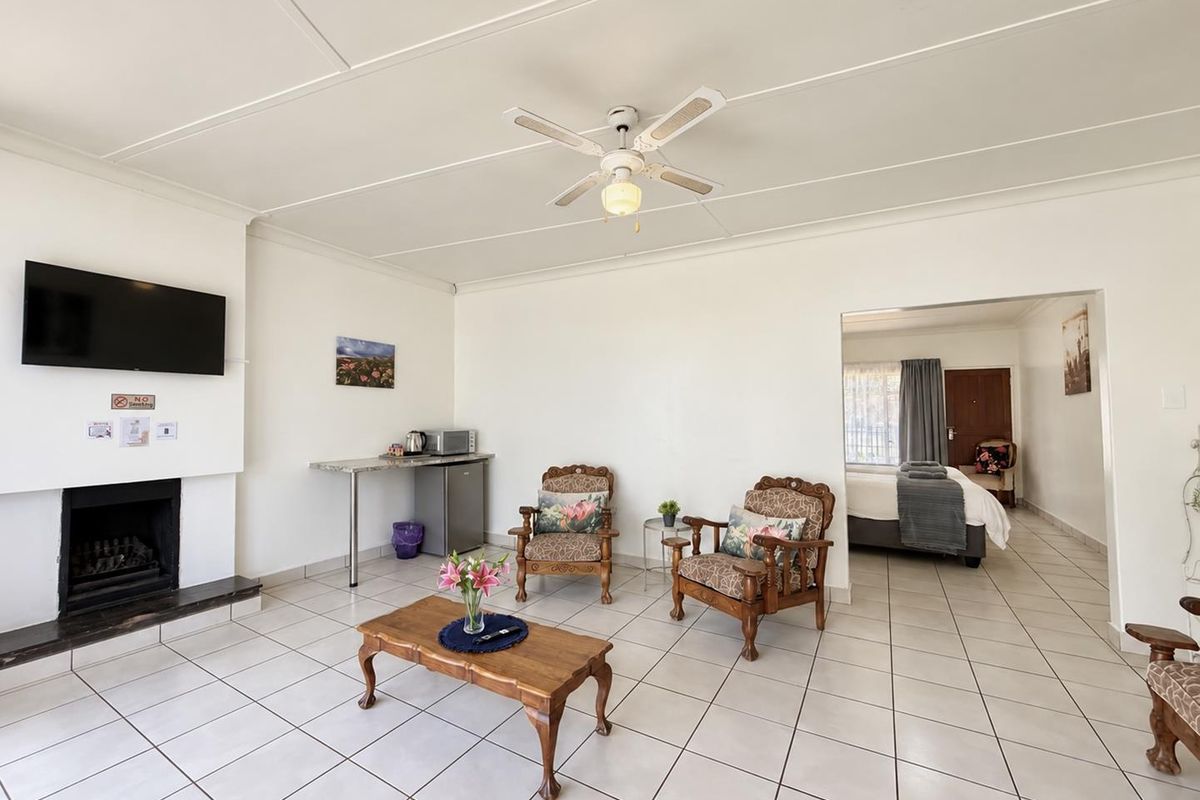 Spacious living area featuring tiled flooring, a built-in fireplace, and a ceiling fan, with an open transition to the adjacent bedroom.