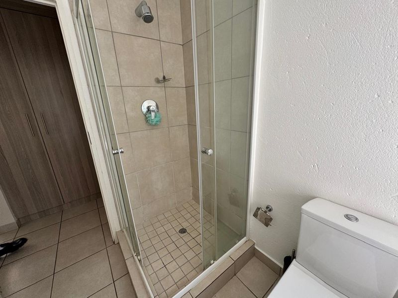 A functional bathroom featuring a glass-enclosed shower, tiled flooring, and a modern toilet, with adjacent built-in storage cabinetry.