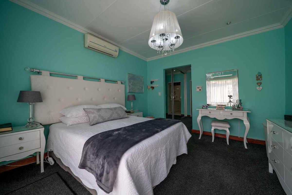 A spacious bedroom featuring a wall-mounted air conditioning unit, crown molding, and an en-suite bathroom entrance with mirrored sliding doors.