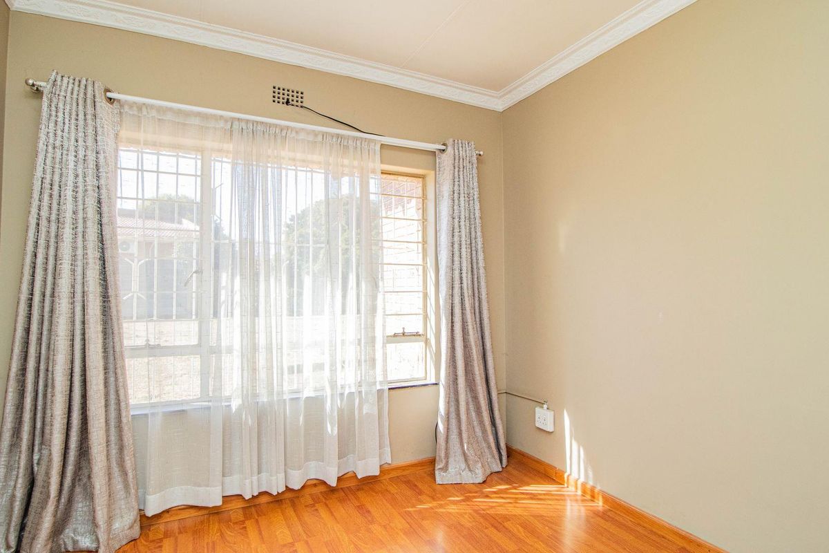 A bright bedroom featuring warm-toned laminate flooring, decorative crown molding, and a large window fitted with security bars.