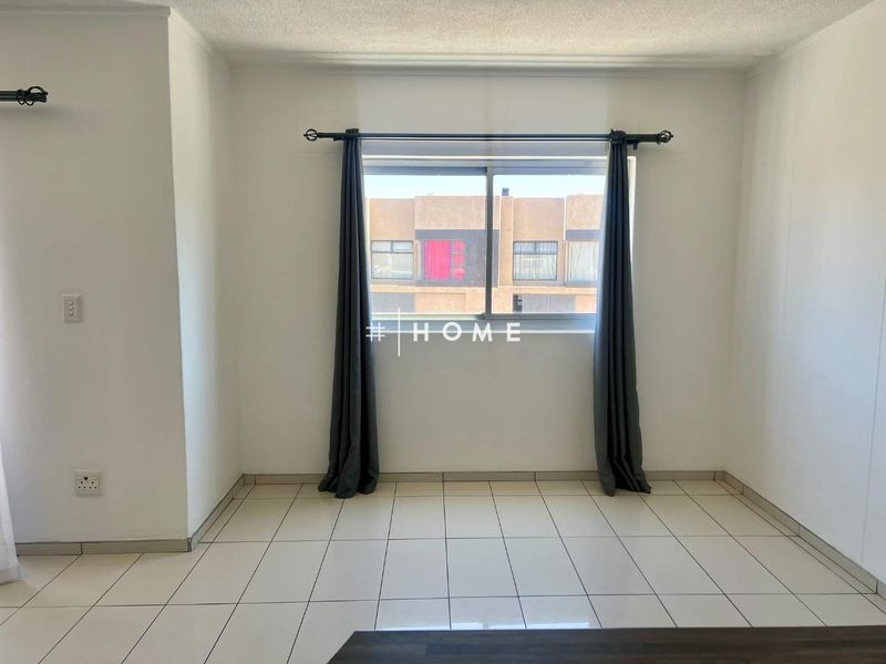 A bright, empty bedroom featuring neutral tiled flooring and a large sliding window, providing a clean canvas for personalization.