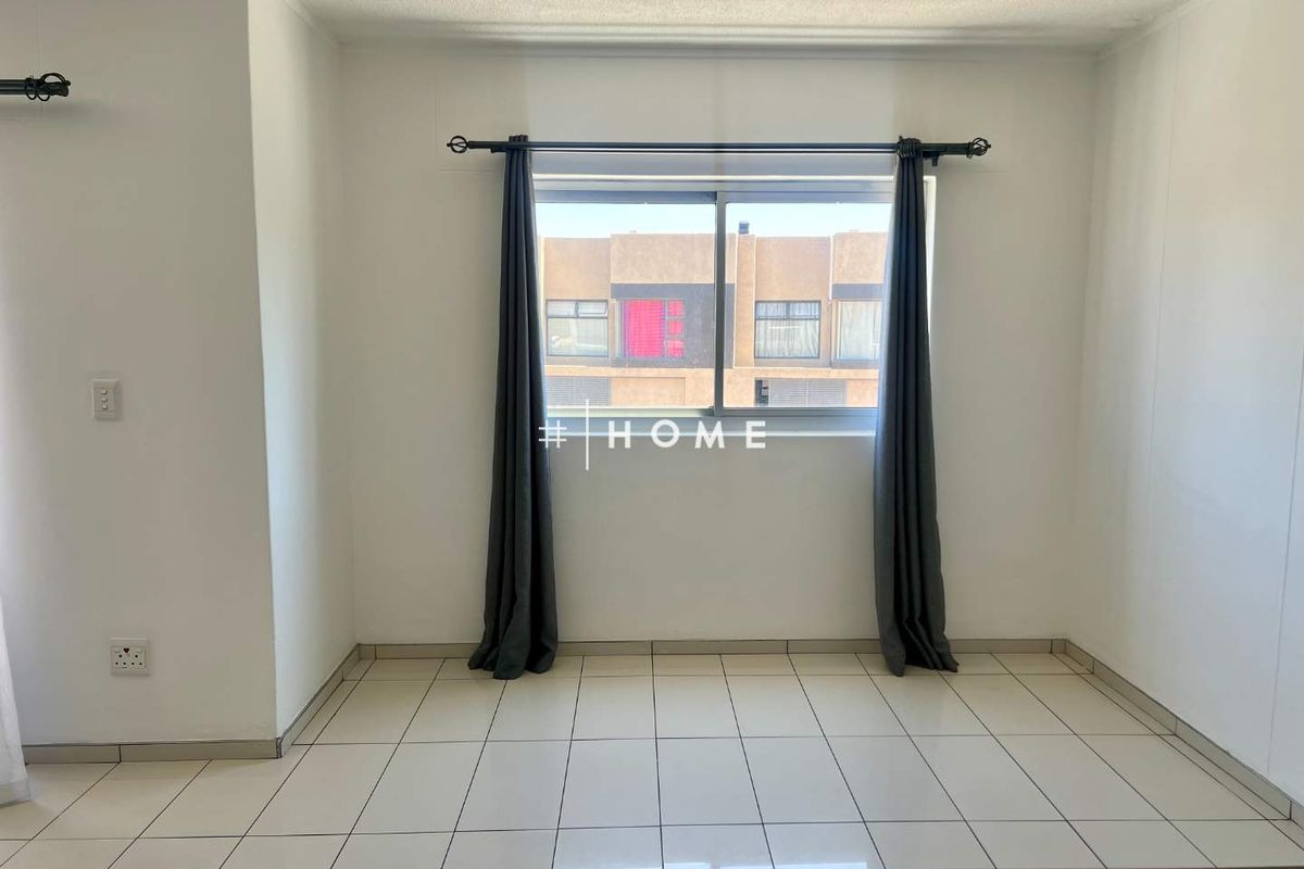 A bright, empty bedroom featuring neutral tiled flooring and a large sliding window, providing a clean canvas for personalization.