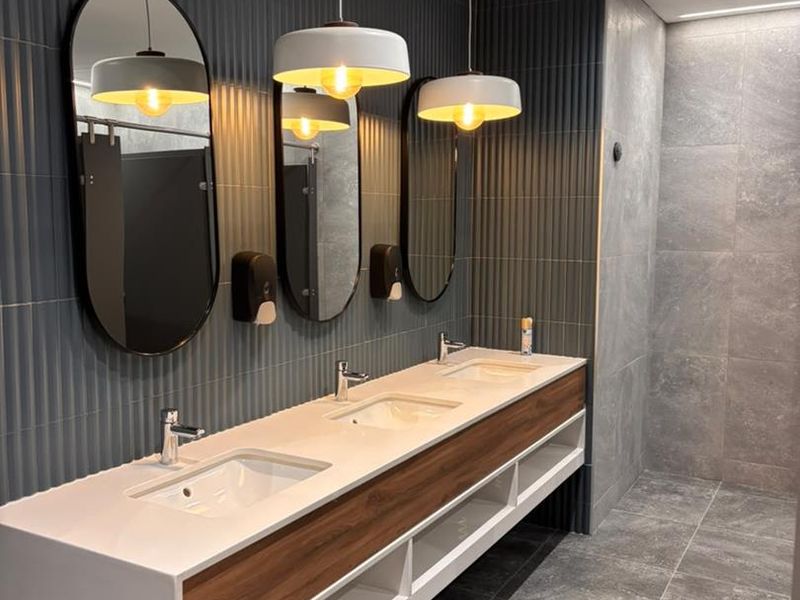 Modern office bathroom featuring a sleek triple vanity with integrated sinks, fluted wall tiling, and contemporary pendant lighting.