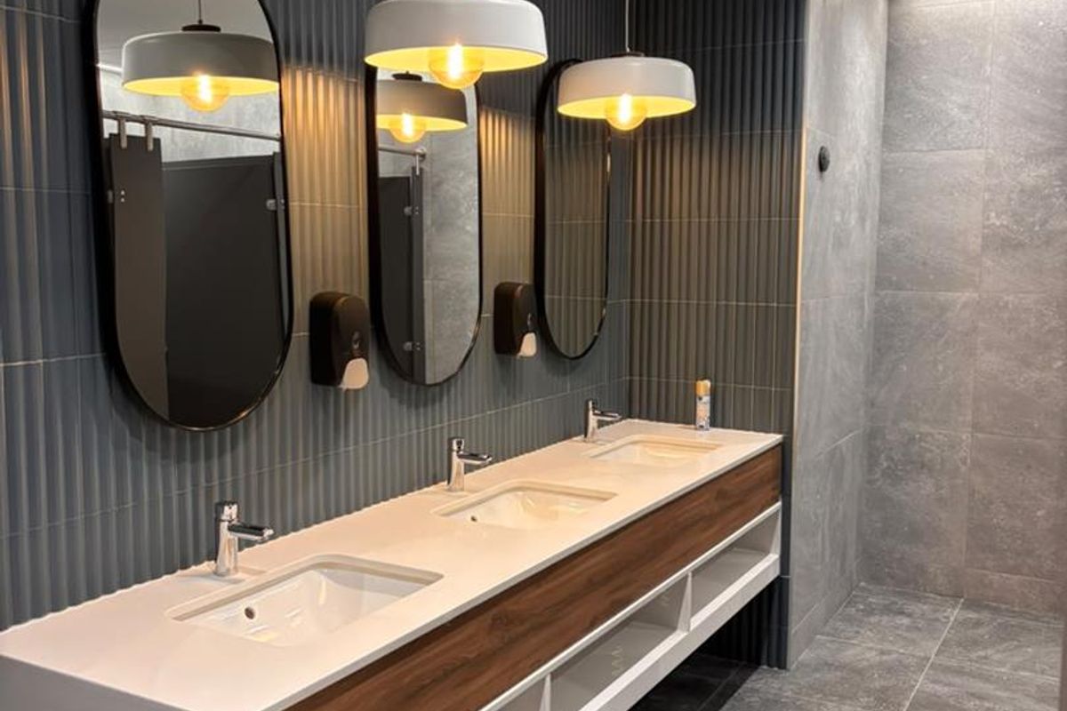 Modern office bathroom featuring a sleek triple vanity with integrated sinks, fluted wall tiling, and contemporary pendant lighting.
