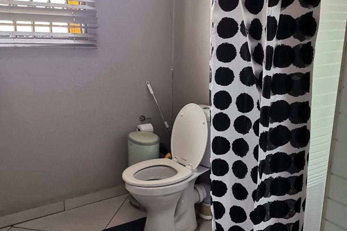 A functional bathroom featuring a standard toilet, tiled flooring, and a window with fitted blinds.