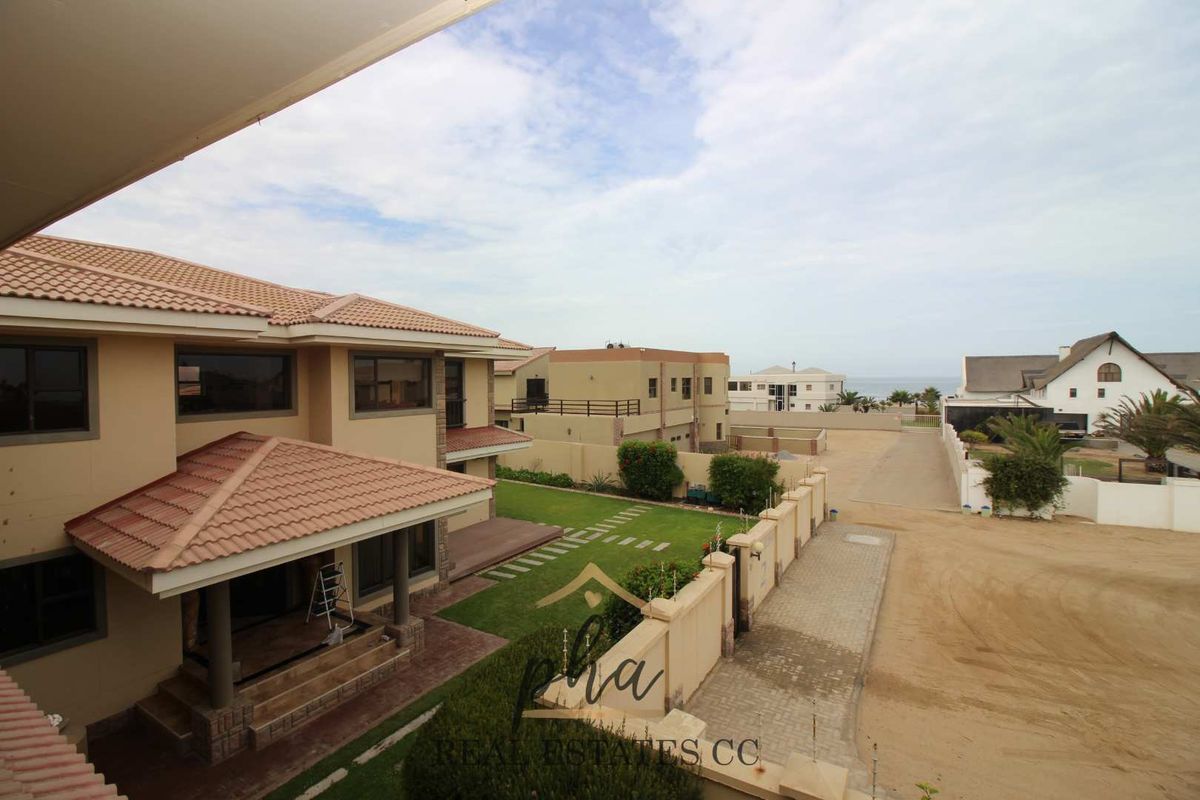Elevated view of the property exterior, showcasing the tiled roof, covered patio, landscaped garden, and surrounding residential estate with distant sea views.