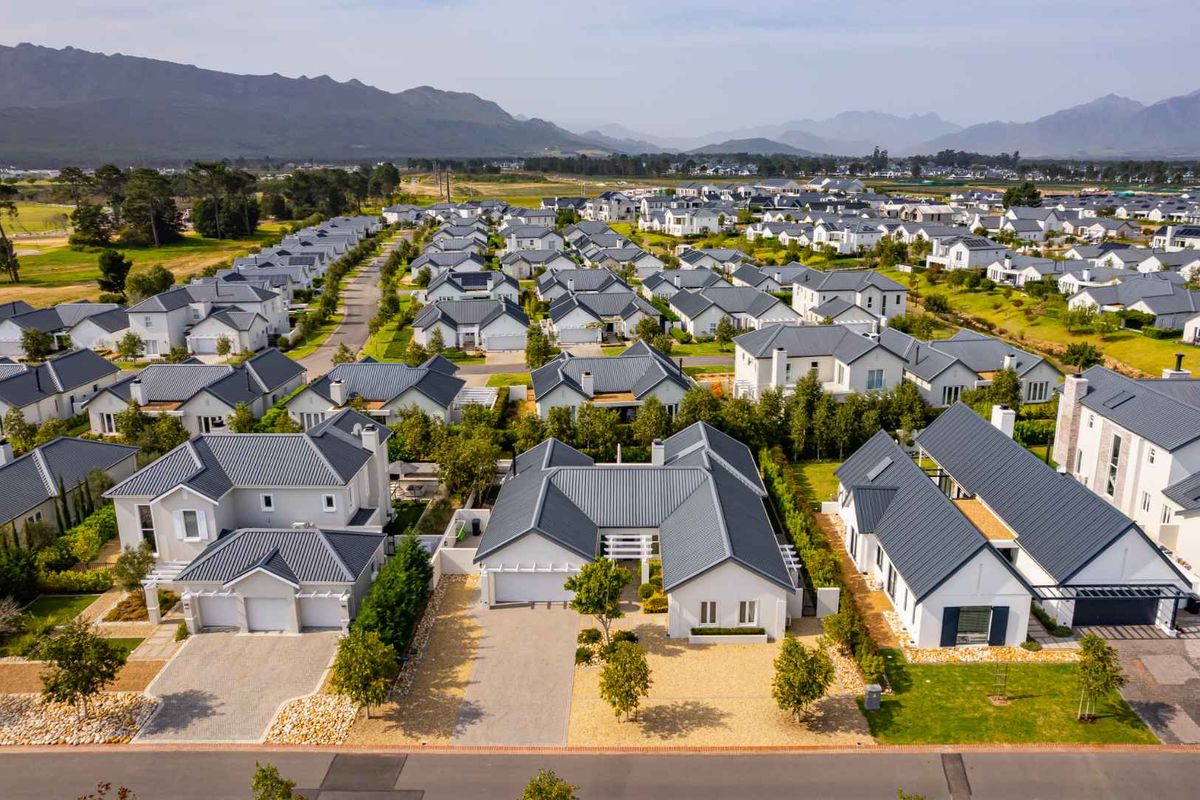 An aerial view of a modern residential estate featuring uniform architectural styles, pitched metal roofs, and well-maintained landscaped surroundings.