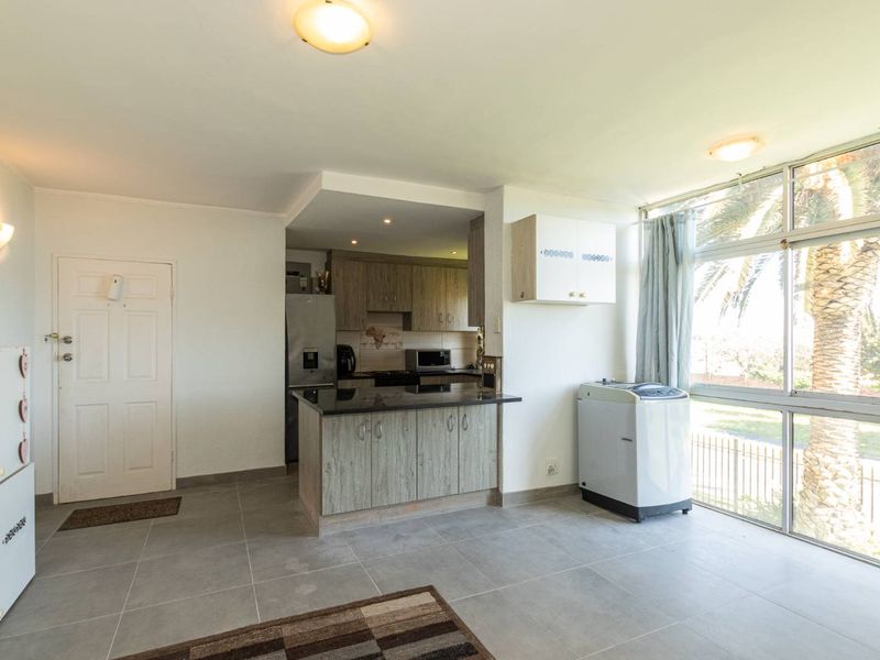 Open-plan kitchen and living area featuring modern cabinetry, granite countertops, tiled flooring, and large windows providing ample natural light.