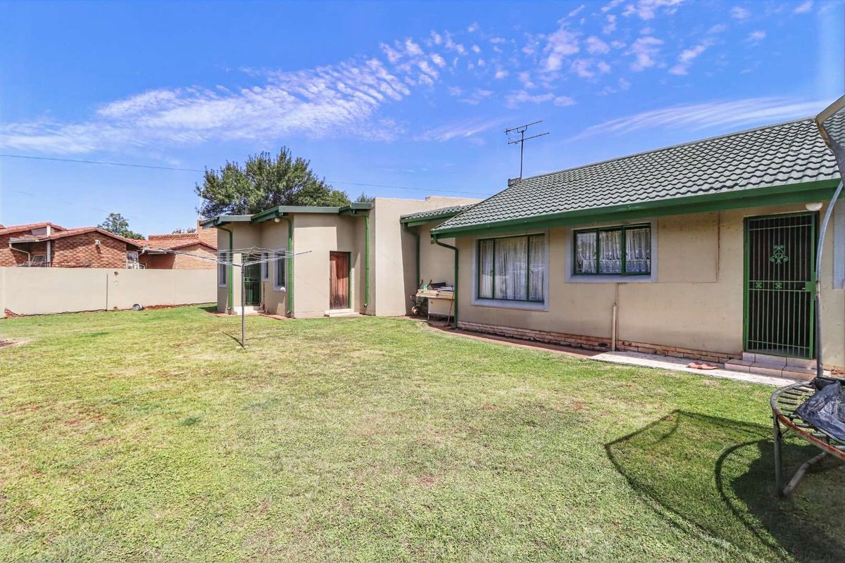 A view of the rear exterior of the house featuring a lawn, tiled roof, and security gates on the doors and windows.