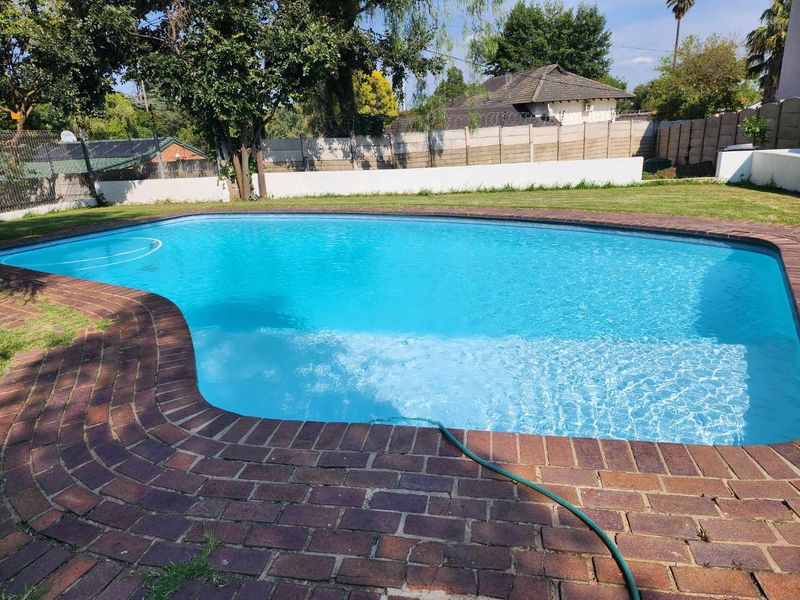 A well-maintained swimming pool area featuring brick coping and surrounding paving, set within a private garden with a secure boundary wall.
