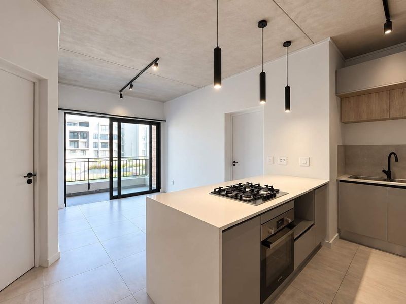 Modern open-plan kitchen and living area featuring a central island with gas hob, sleek cabinetry, and sliding doors leading to a private balcony.
