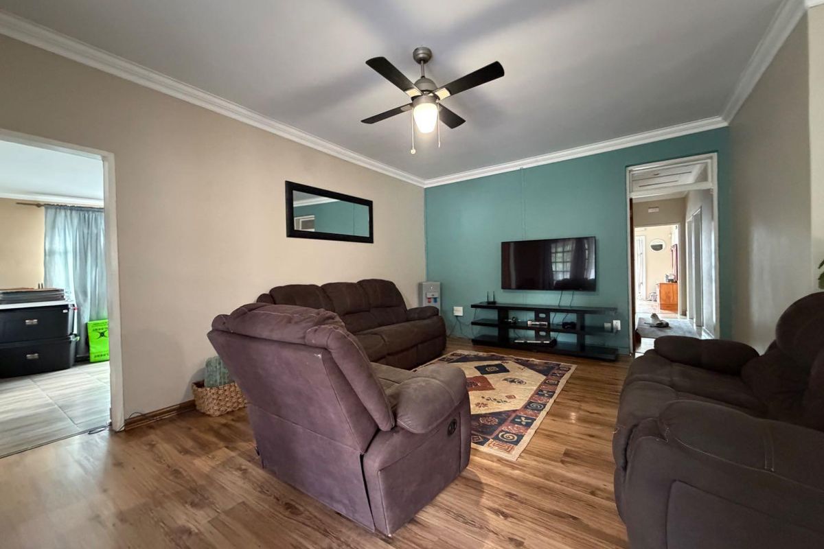 A living room featuring wood-look flooring, a ceiling fan, and a teal accent wall, providing a comfortable and functional living space.