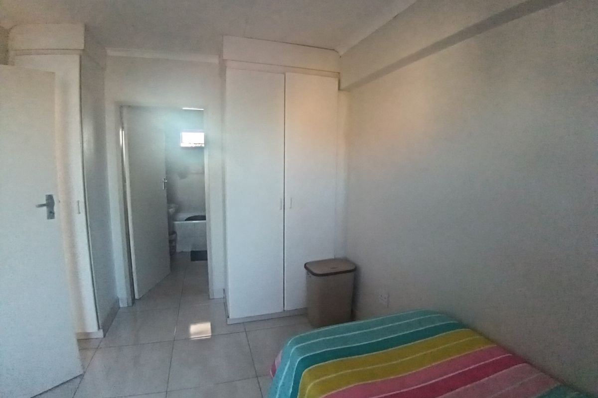 A bedroom featuring built-in cupboards, tiled flooring, and a coved ceiling, with an adjacent bathroom visible through the doorway.