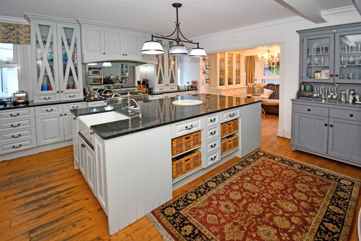 A well-appointed kitchen featuring a large central island with a farmhouse sink, granite countertops, custom cabinetry, and hardwood flooring.
