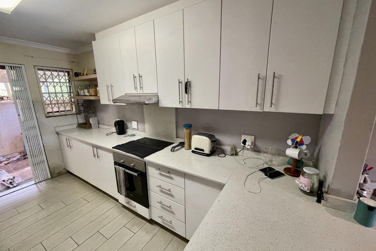 A functional kitchen featuring white cabinetry, stone-look countertops, a built-in oven, and a hob with an extractor fan.