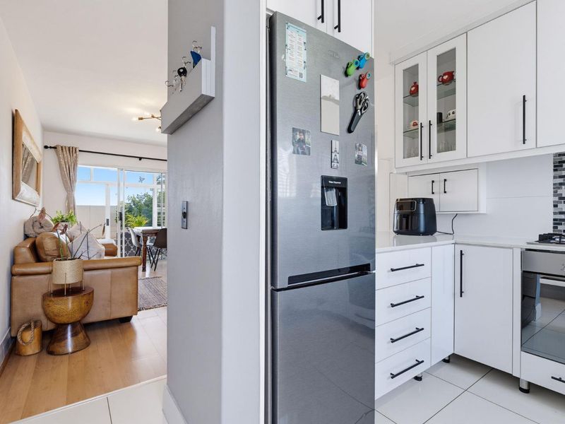 Open-plan kitchen and living area featuring modern white cabinetry, integrated appliances, tiled kitchen floors, and seamless flow to a bright living space.