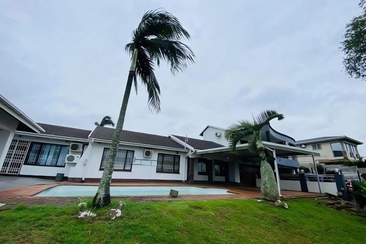 Rear exterior view of the house featuring a swimming pool, covered patio area, and established garden with mature palm trees.