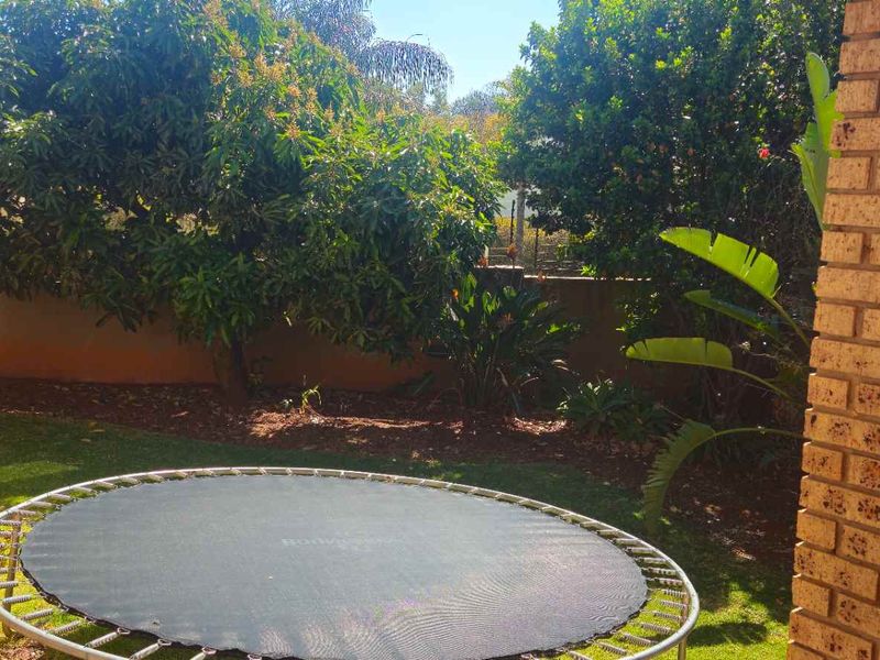 A private garden area featuring a brick pillar, established trees, and a lawn, enclosed by a boundary wall.