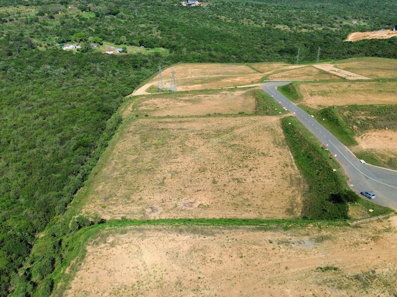 Aerial view of a cleared industrial land parcel with direct access to a paved road and surrounding natural vegetation.