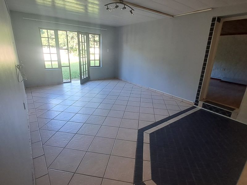 An empty living room featuring tiled flooring, a ceiling-mounted light fixture, and french doors providing access to the exterior.
