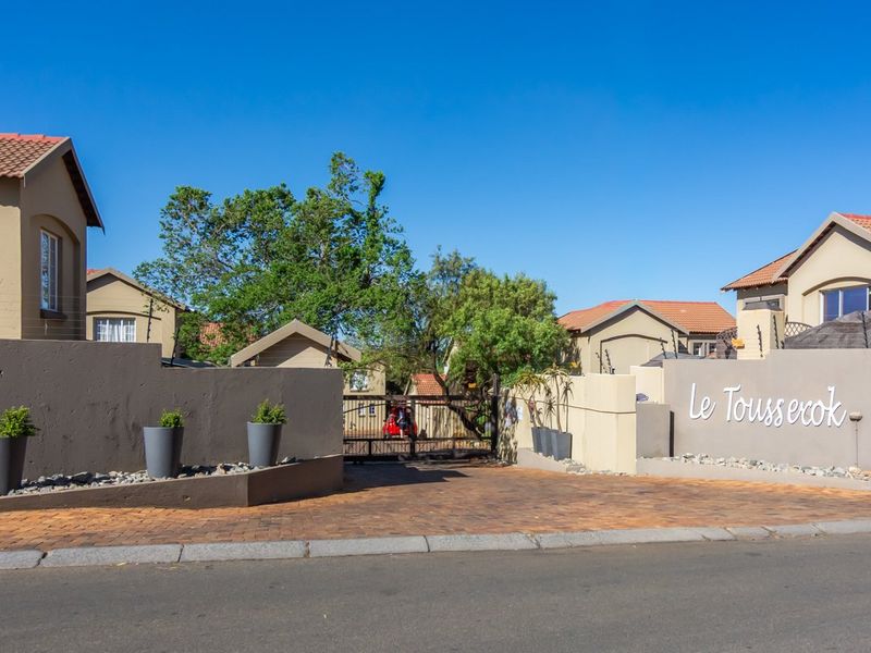 Front entrance view of Le Toussrok townhouse complex featuring a paved driveway, secure gated access, and perimeter walling with electric fencing.