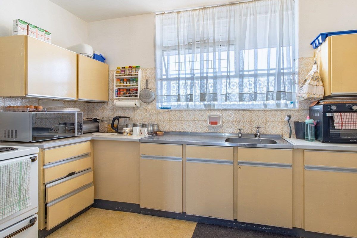 A dated kitchen featuring original laminate cabinetry, a stainless steel sink, and patterned wall tiles, offering significant potential for a modern renovation.