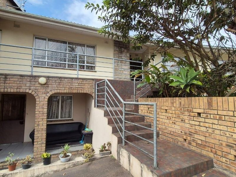 Front elevation of a multi-level brick house featuring a tiled staircase, metal railings, and a covered patio area.