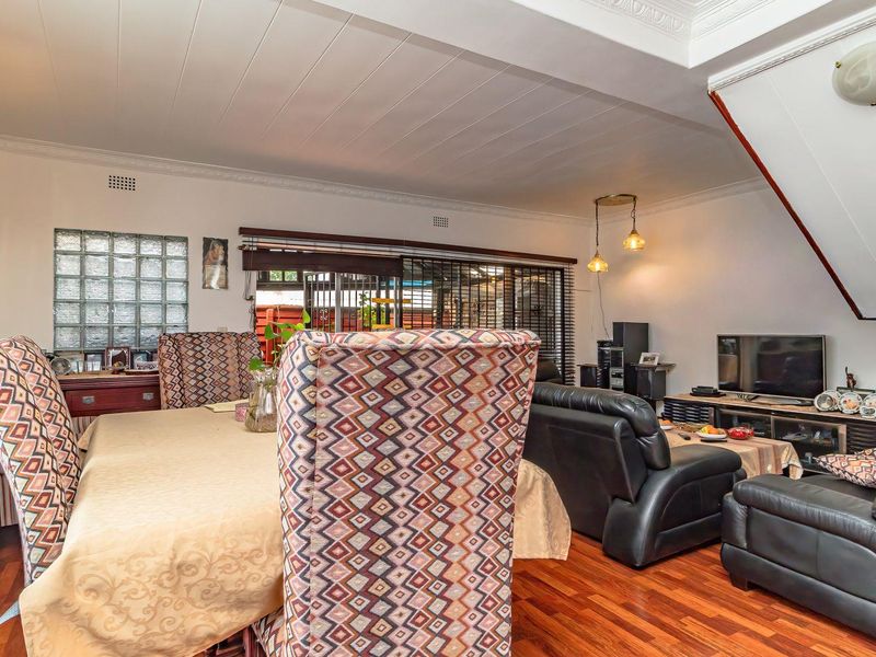 Open plan living and dining area featuring hardwood flooring, crown molding, and a glass block window, providing a functional and connected living space.