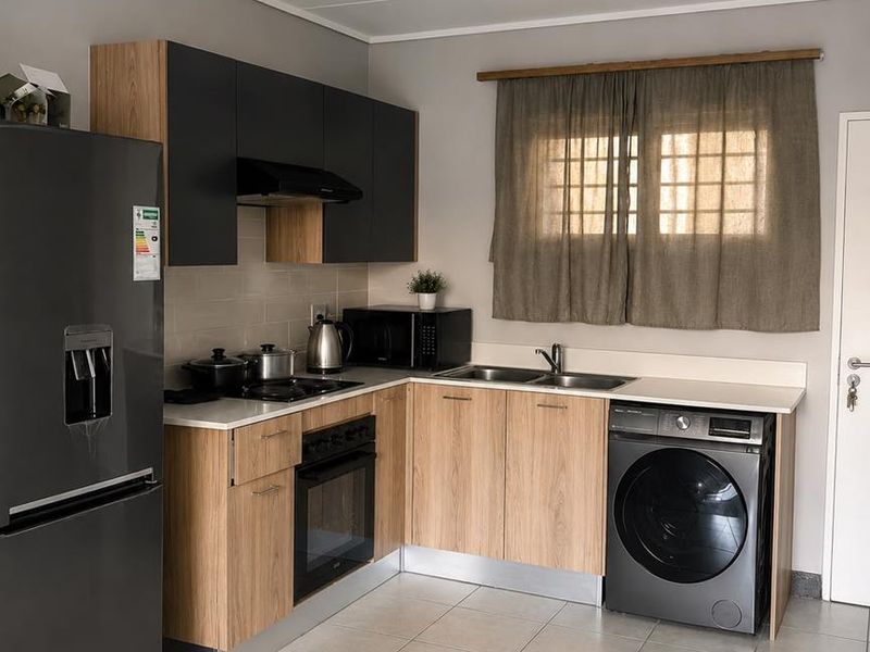 Modern kitchen featuring wood-finish cabinetry, contrasting dark upper cupboards, integrated appliances, tiled flooring, and a functional layout with dedicated laundry space.