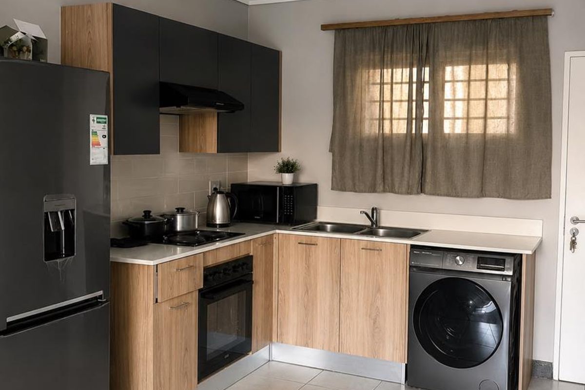 Modern kitchen featuring wood-finish cabinetry, contrasting dark upper cupboards, integrated appliances, tiled flooring, and a functional layout with dedicated laundry space.