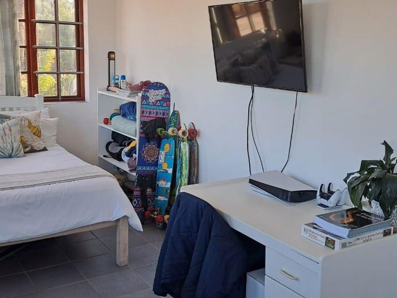 A bedroom featuring tiled flooring, a large window providing natural light, and a wall-mounted television.