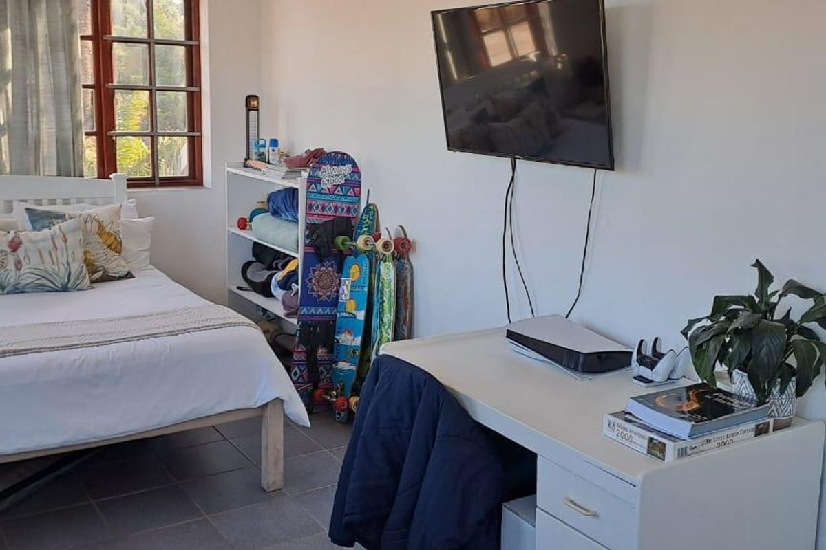 A bedroom featuring tiled flooring, a large window providing natural light, and a wall-mounted television.