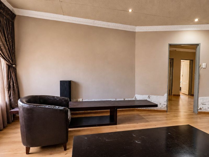 Living room featuring laminate flooring, recessed lighting, and decorative ceiling cornicing, currently showing signs of wall surface wear and peeling paint.
