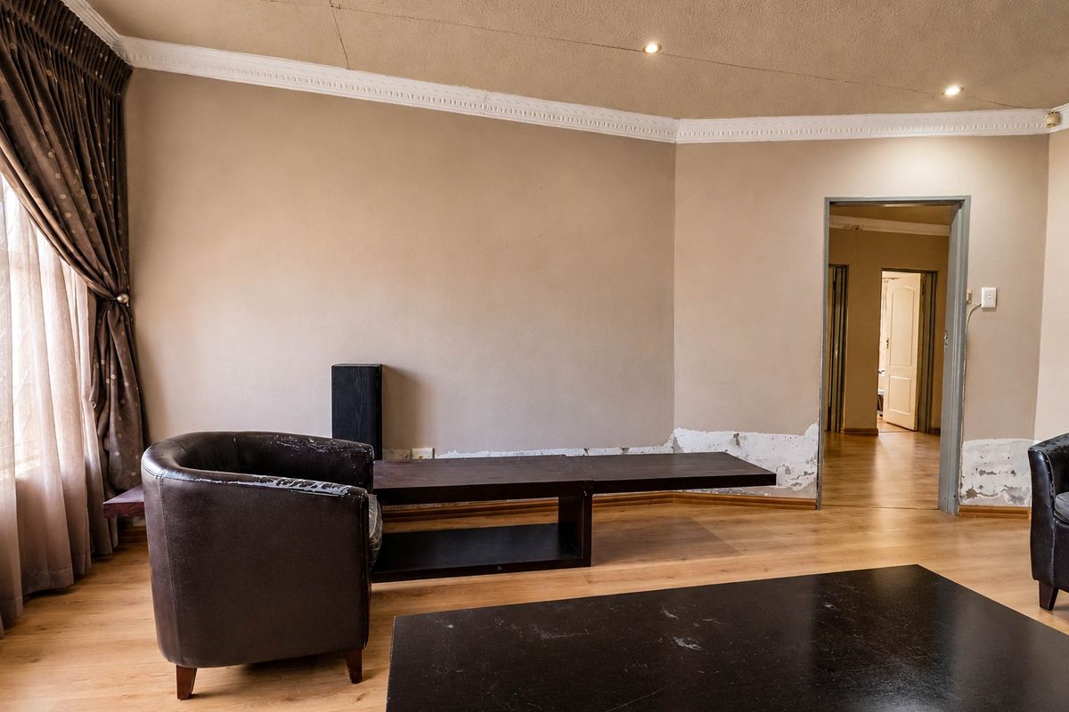 Living room featuring laminate flooring, recessed lighting, and decorative ceiling cornicing, currently showing signs of wall surface wear and peeling paint.