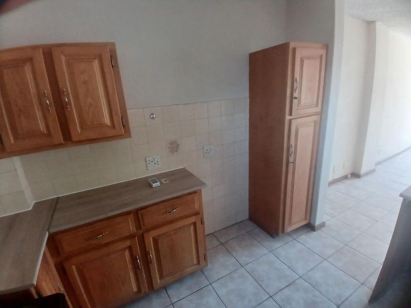 A dated kitchen area featuring wooden cabinetry, laminate countertops, and tiled flooring, offering a functional layout ready for modernization.